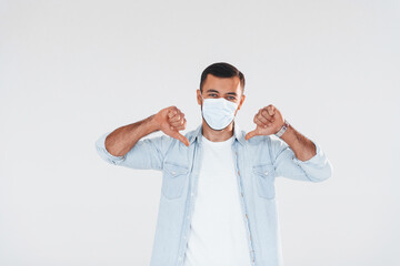 In protective mask. Young handsome man standing indoors against white background