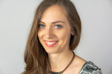 studio portret of long brown hair young beautiful girl with big smile and white teeth  wearing white grey patterned dress and a neckless on a light grey background  © michnik101