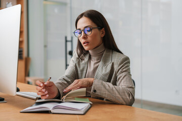 Focused charming woman in eyeglasses working with computer and planner