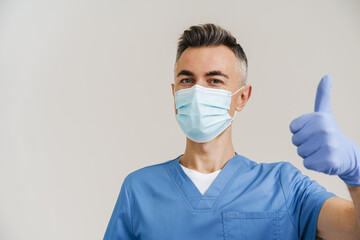 Pleased white-haired medical doctor in face mask and gloves showing thumb up