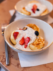 Traditional russian ukrainian dish for breakfast syrniki. Cottage cheese pancakes, ricotta fritters on ceramic plate with sour cream and fresh berries blueberries and strawberries on beige marble