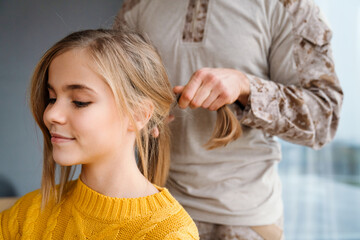 Fototapeta premium Masculine military man doing hair of his smiling daughter at home
