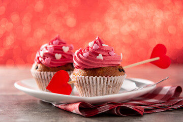Cupcake decorated with sugar hearts and a cupid arrow for Valentine's Day on wooden table and red background
