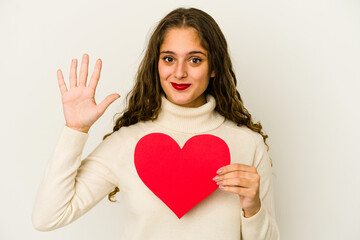 Young caucasian woman holding a heart valentines day shape isolated smiling cheerful showing number five with fingers.