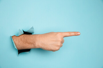 Male hand making sign through a hole in paper isolated on blue background.