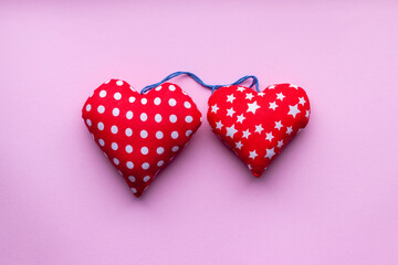 Two soft red hearts with white circles and stars tied with a blue rope on pink background