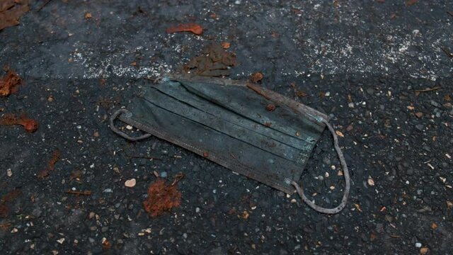 Dirty trampled disposable medical mask on the ground in mud, falled leaves around