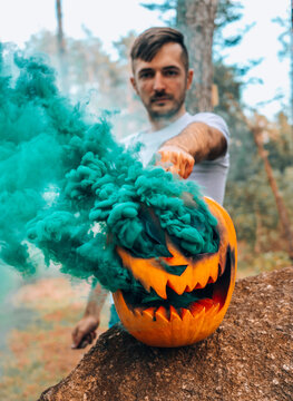 orange pumpkin on hallown from which there is colored smoke in the hands of a man in the forest