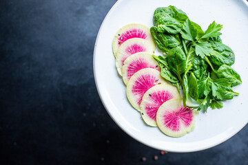 Watermelon radish fresh salad chinese daikon Slices pink fruit, green leaves spinach lettuce on the table healthy meal snack top view copy space food background keto or paleo diet