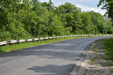 A long turn of an asphalt road with a metal fence.