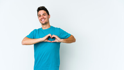 Young caucasian man isolated on white background smiling and showing a heart shape with hands.