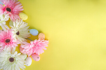 Easter greeting card background with gerbera flowers and colorful easter eggs. Top view flat lay on yellow background copy space for text