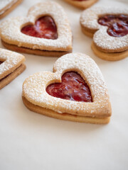 Homemade heart shaped cookies with raspberry jam sprinkled with icing sugar on white background in morning light