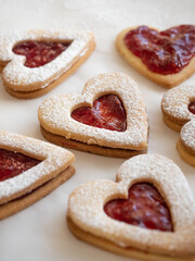 Obraz na płótnie Canvas Homemade heart shaped cookies with raspberry jam sprinkled with icing sugar on white background in morning light