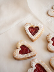 Homemade heart shaped cookies with raspberry jam sprinkled with icing sugar on white background in morning light