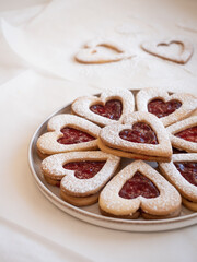 Homemade heart shaped cookies with raspberry jam sprinkled with icing sugar on white background in morning light