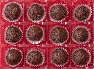 balls of chocolate with black chocolate chips in a rectangle transparent box on red background, above view