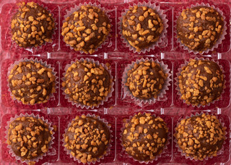 balls of chocolate with peanut praline in a rectangle transparent box on red background, above view