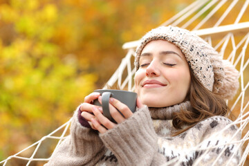 Relaxed woman smelling coffee on hammock in autumn