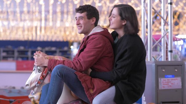 happy romatic couple swinging on the carousel horse at christmas time