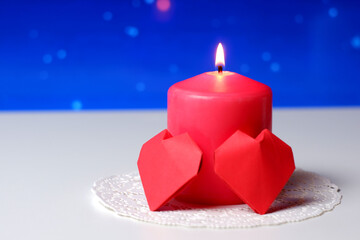 Couple of 3D red paper hearts, burning pink candle on white openwork paper napkin, blue bokeh snow background closeup view selective focus. Love, Valentine's, women's day, relations, romantic concept