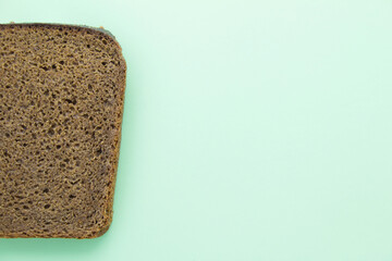 Slice of brown rye bread on green paper background with copy space for text.