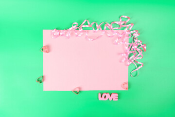 Pink copied space on a green background, next to hearts, serpentine and the inscription LOVE on a green background.