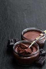 Dark chocolate mousse with ganache in glass jar on black stone background