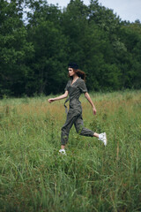 Woman in the field runs on the grass in a green jumpsuit 