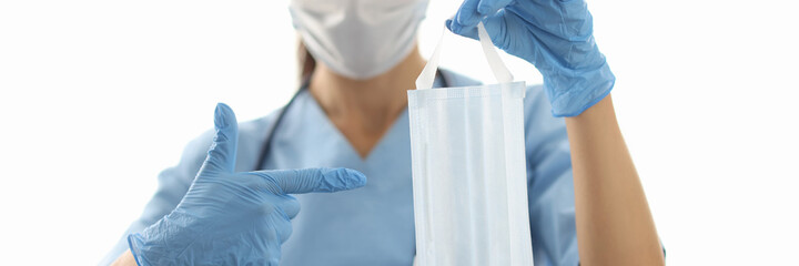 Fototapeta premium Female doctor holding face protective mask in rubber gloves and pointing finger close-up. Covid-19 prevention concept