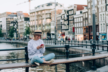 Young smiling female surfing smartphone on bench on embankment