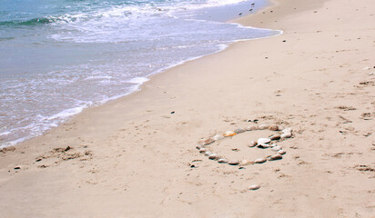 Heart made of sea shells on a beach sand, summer background on a beautiful summer day.