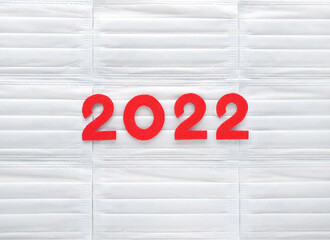 Red felt new year numbers 2022 on white medical masks background. Coming future. Place for your...