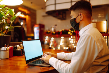 Young business man working from home with laptop, wearing protective mask. Self-isolation and prevention of coronavirus, remote work. Covid-2019. Technology, business, freelance concept.