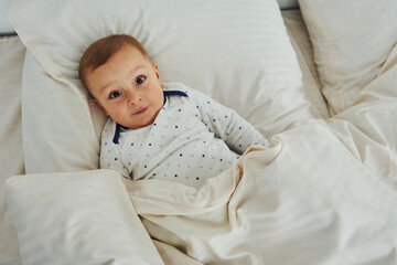 Cute little boy is on the bed. Interior and design of beautiful modern bedroom at daytime