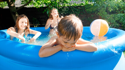 Portrait of upset little boy sitting on the poolside while family playing and having fun. Concept of happy and cheerful summer holidays and vacation