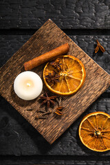 Winter spices concept. Flat lay view of various spices: cinnamon stick, clove, star anise, dried orange slices. Wood plate with seasonal potpourri on dramatic black burnt wood background.