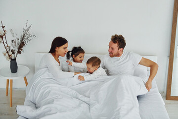 Woman and man lying down on bed with their children. Interior and design of beautiful modern bedroom at daytime