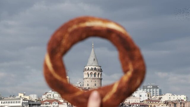 Traditional Turkish bagel simit in a female hand from inside the Galata Tower with other buildings are visible at Istanbul 2x slow motion