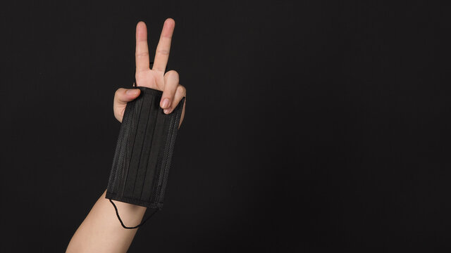 Hand is hold black medical face mask and doing Victory or Peace hand Sign on black background.isolated, copy space.