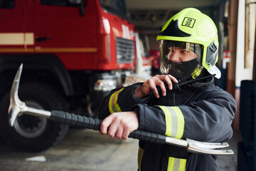 Male firefighter in protective uniform standing near truck