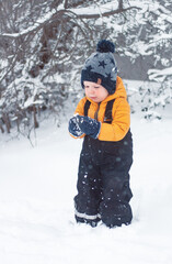 Fototapeta na wymiar a little boy stands in the outdoor and looks in surprise at the snow in his hands