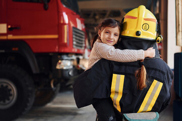 Happy little girl is with female firefighter in protective uniform