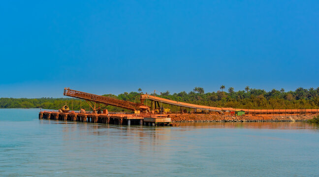 Outdoor industrial jetty at river bank with incline large conveyor for transportation bauxite ore from mining shuttle trains to feeder ships. Guinea, West Africa.