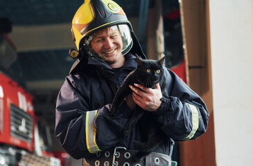 Portrait of firefighter in protective uniform that holds cute little black cat