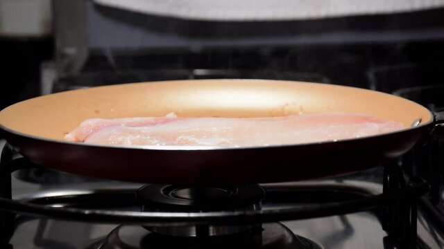 Tilapia fish fillet (Saint Peter) being placed in a hot frying pan with butter.