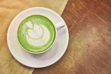 Cup of matcha latte on wooden background and a beige napkin in a cafe with copy space. High quality photo