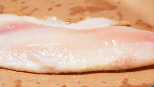 Closeup of tilapia fillet (Saint Peter) being fried in butter (side tracking).