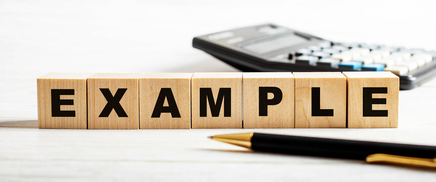 On a light background, a pen, calculator and wooden cubes with the inscription EXAMPLE. Defocus