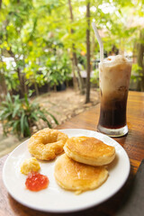 Delicious pancakes and croissant with jam and iced coffee on wooden table in garden background. 